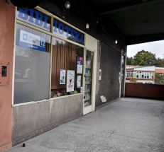 Na zdjęciu widać przeszkloną witrynę, na niej plakaty, oznaczenie filii, duży napis: „BIBLIOTEKA”. Dalej drzwi wejściowe, na nich tabliczka z godzinami otwarcia, nad drzwiami tabliczka z numerem filii. Wejście jest zadaszone.