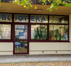 Na zdjęciu żółty, parterowy budynek, przed budynkiem chodnik i brukowana droga, wejście jest zadaszone. Na drzwiach tabliczki z godzinami otwarcia oraz oznaczeniem filii.